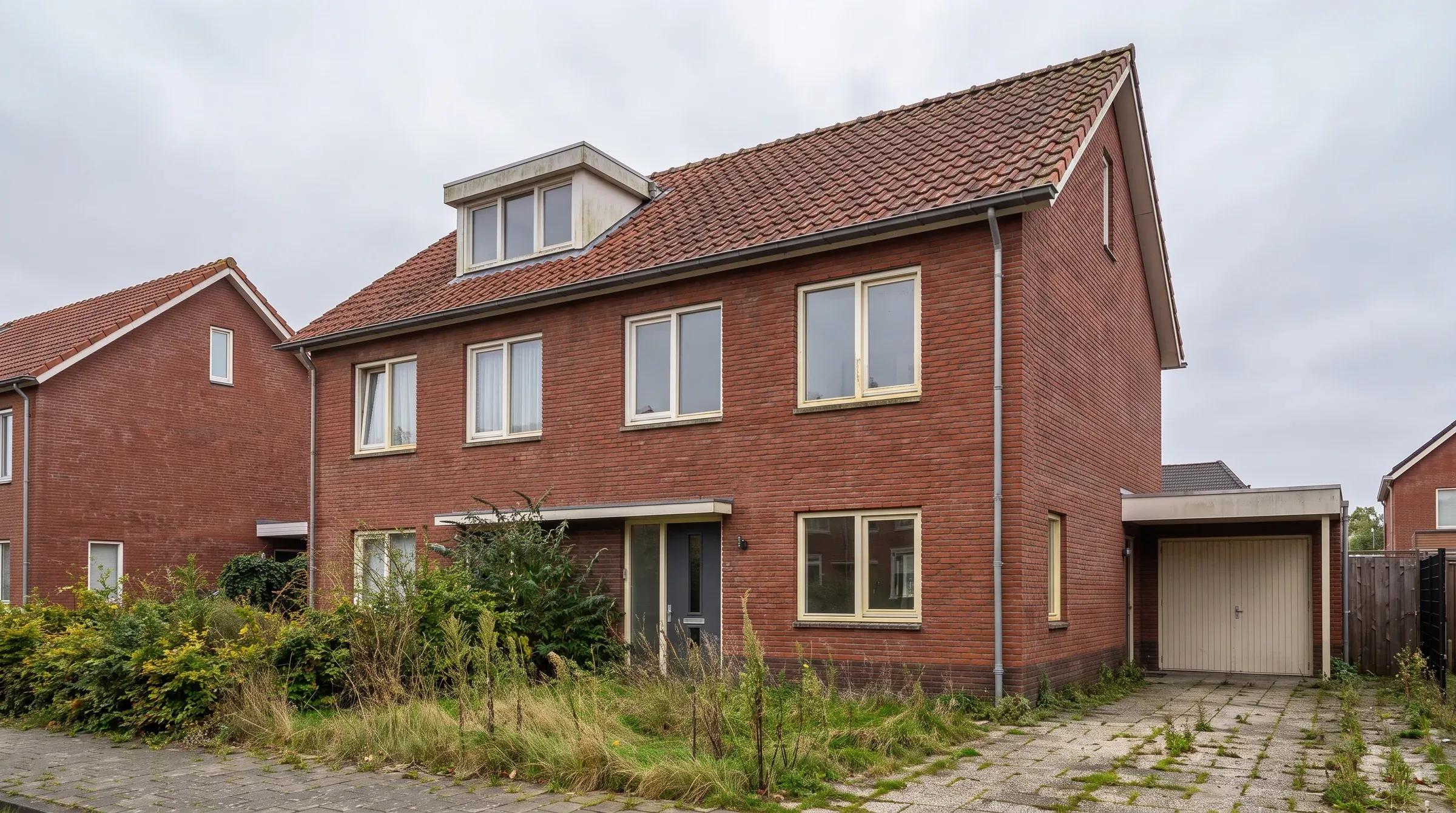 Dezelfde woning vóór de verbouwing: gedateerde kozijnen, geen zonnepanelen en een verwaarloosde tuin